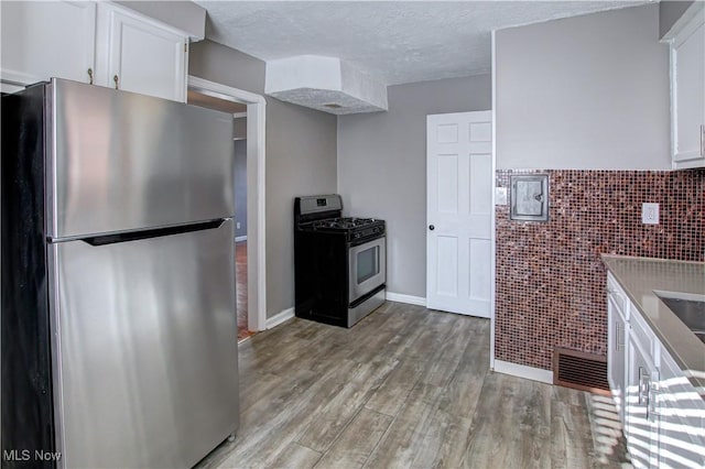 kitchen featuring light wood-type flooring, tile walls, white cabinets, stainless steel appliances, and a textured ceiling