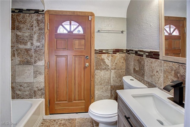 bathroom with tile walls, a bath, vanity, and toilet