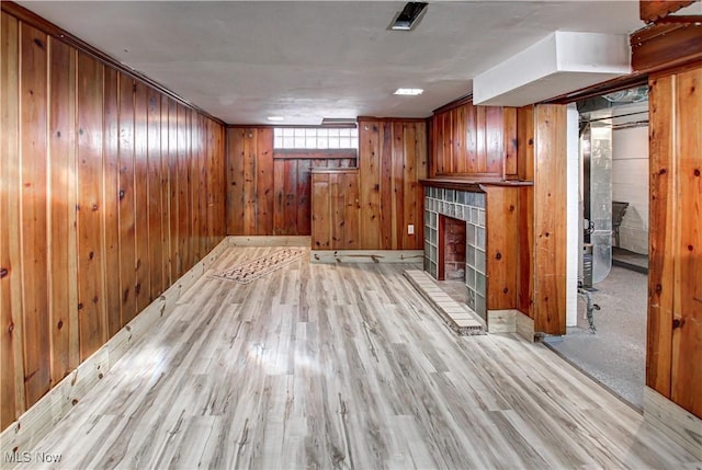 unfurnished living room with light hardwood / wood-style flooring, a fireplace, and wooden walls