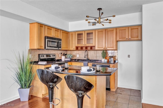 kitchen featuring a textured ceiling, appliances with stainless steel finishes, an inviting chandelier, sink, and a breakfast bar area