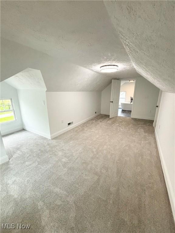 bonus room featuring vaulted ceiling, light colored carpet, and a textured ceiling