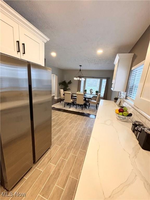 kitchen featuring white cabinetry, an inviting chandelier, hanging light fixtures, stainless steel refrigerator, and light stone countertops