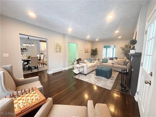 living room with dark wood-type flooring, a chandelier, and a textured ceiling