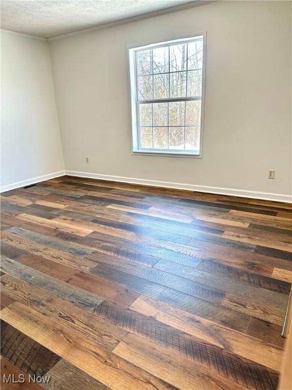 empty room featuring a textured ceiling, dark hardwood / wood-style flooring, and ornamental molding