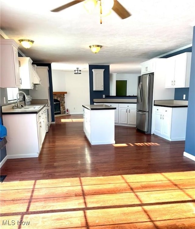 kitchen with sink, stainless steel refrigerator, dark wood-type flooring, a stone fireplace, and white cabinets