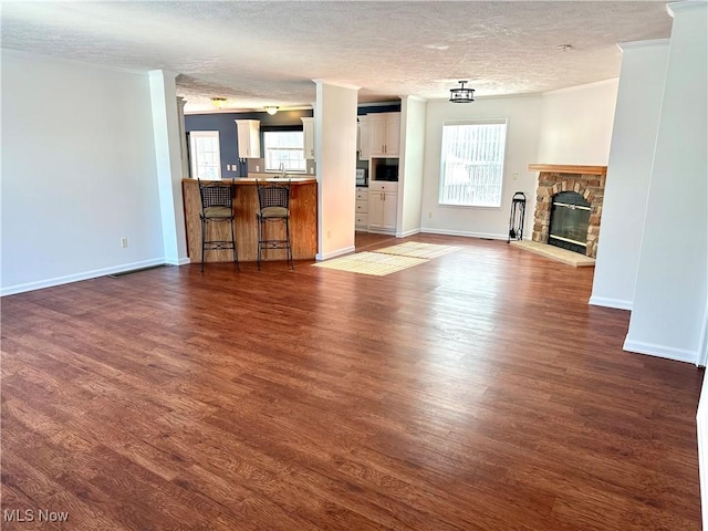 unfurnished living room with dark wood-type flooring, sink, a stone fireplace, and a textured ceiling