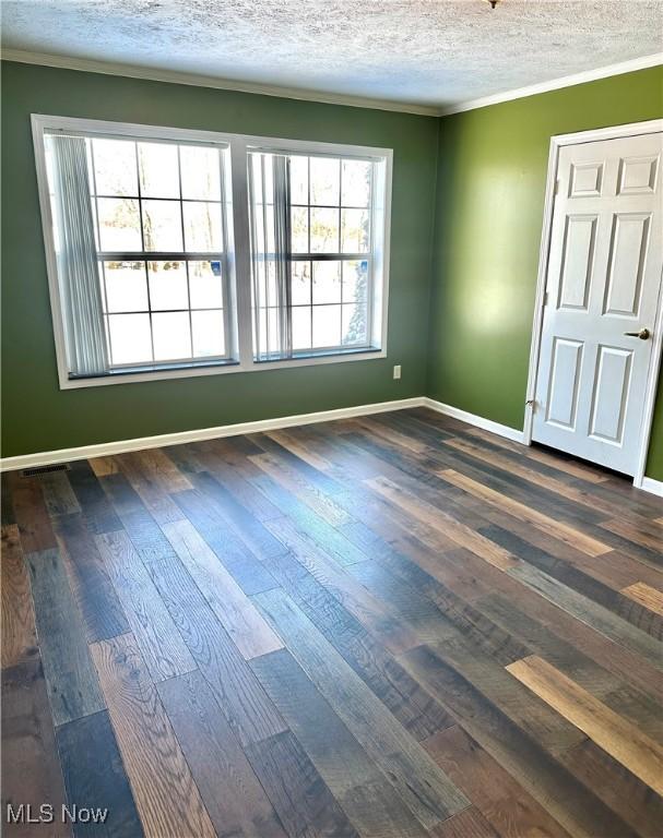 empty room featuring dark wood-type flooring, crown molding, and a textured ceiling