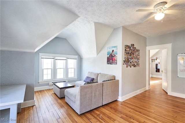 living room featuring ceiling fan, a textured ceiling, light hardwood / wood-style flooring, and lofted ceiling