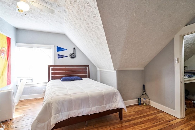 bedroom featuring ceiling fan, wood-type flooring, vaulted ceiling, and a textured ceiling