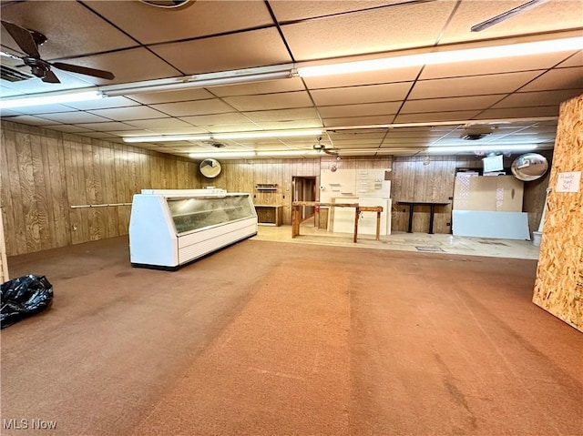 basement featuring ceiling fan, carpet, and wood walls