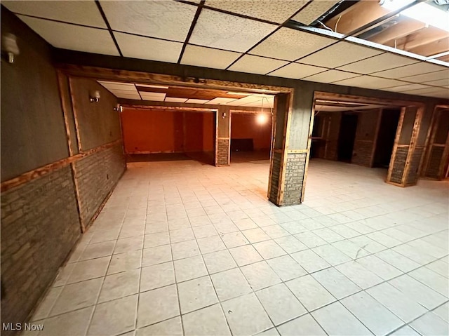 basement with a drop ceiling, brick wall, and wooden walls