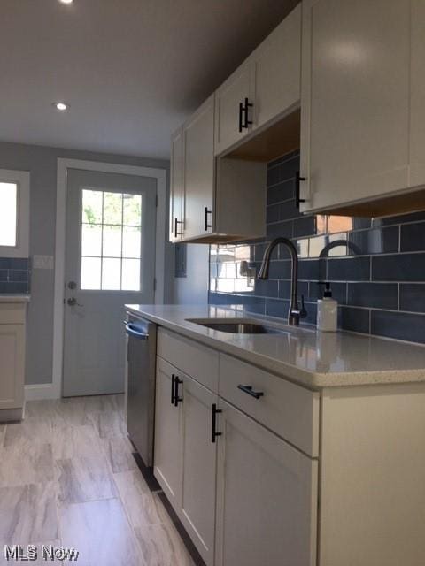 kitchen with white cabinetry, decorative backsplash, stainless steel dishwasher, and sink