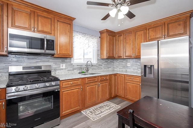 kitchen featuring appliances with stainless steel finishes, sink, light stone counters, and light hardwood / wood-style flooring