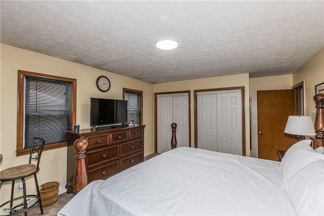 carpeted bedroom featuring a textured ceiling and multiple closets