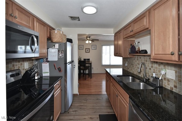 kitchen featuring sink, hardwood / wood-style floors, appliances with stainless steel finishes, and dark stone counters