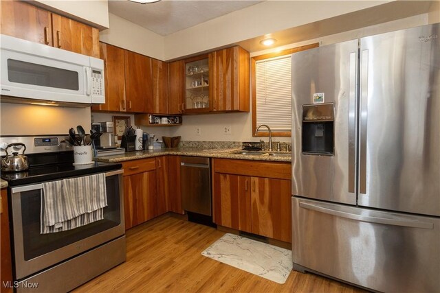 kitchen featuring light wood-type flooring, appliances with stainless steel finishes, sink, and dark stone counters