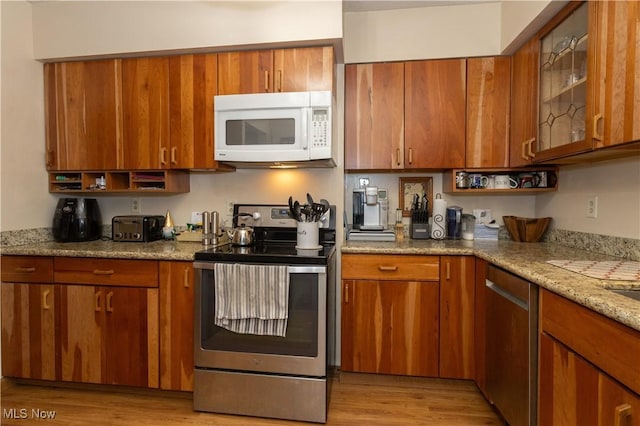 kitchen with appliances with stainless steel finishes, light hardwood / wood-style floors, and light stone counters