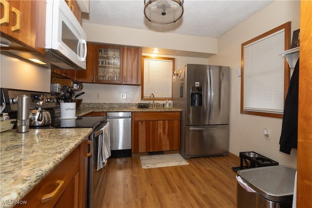 kitchen with light wood-type flooring, light stone countertops, stainless steel appliances, and sink