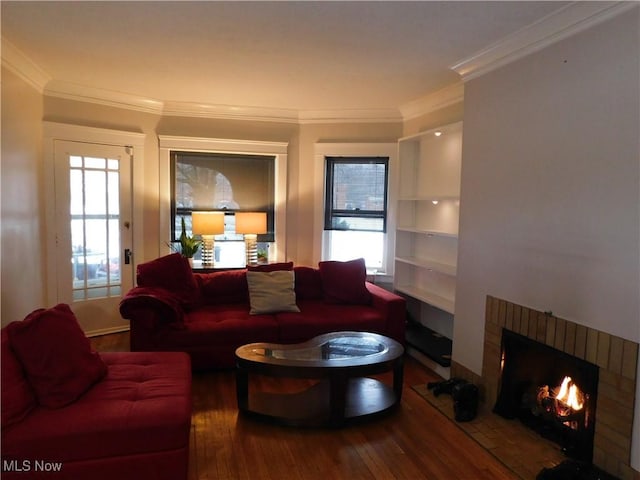 living room with a healthy amount of sunlight, wood-type flooring, a brick fireplace, and crown molding