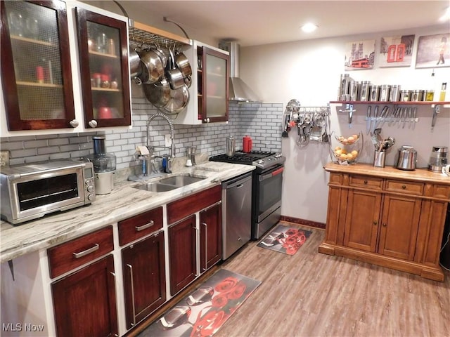 kitchen with appliances with stainless steel finishes, decorative backsplash, light wood-type flooring, wall chimney range hood, and sink