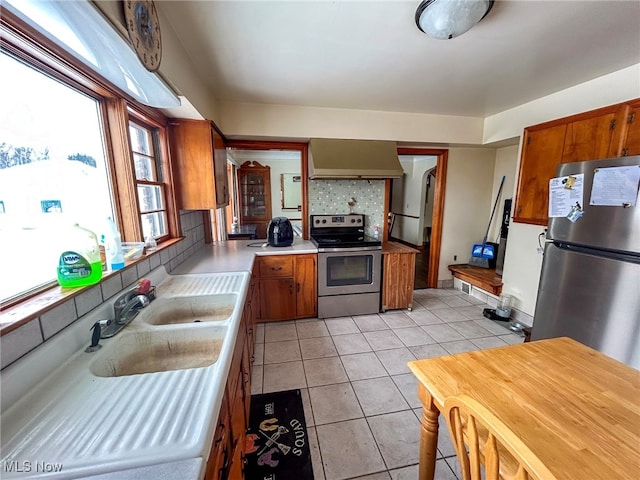 kitchen with light tile patterned floors, stainless steel appliances, backsplash, wall chimney range hood, and sink