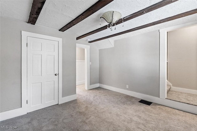 unfurnished bedroom with beam ceiling, ensuite bathroom, a textured ceiling, and carpet flooring