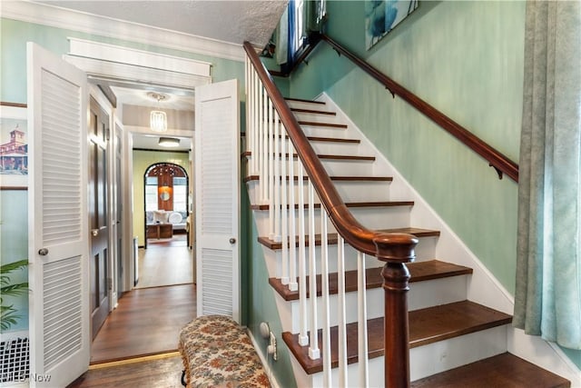 staircase with hardwood / wood-style flooring, a textured ceiling, and ornamental molding