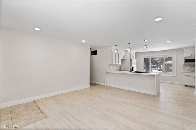 kitchen featuring white cabinetry, kitchen peninsula, appliances with stainless steel finishes, decorative backsplash, and decorative light fixtures