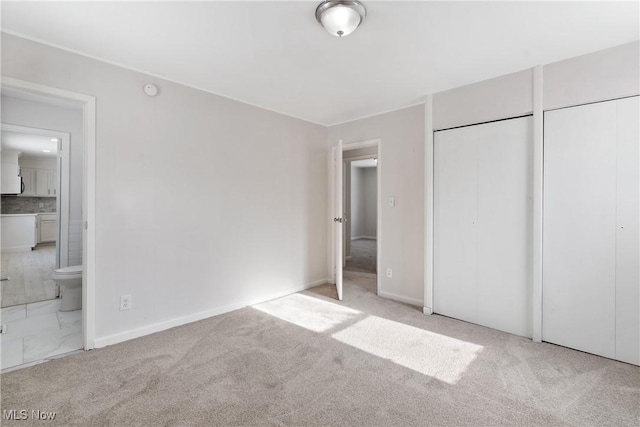 unfurnished bedroom with a closet, ensuite bathroom, and light colored carpet