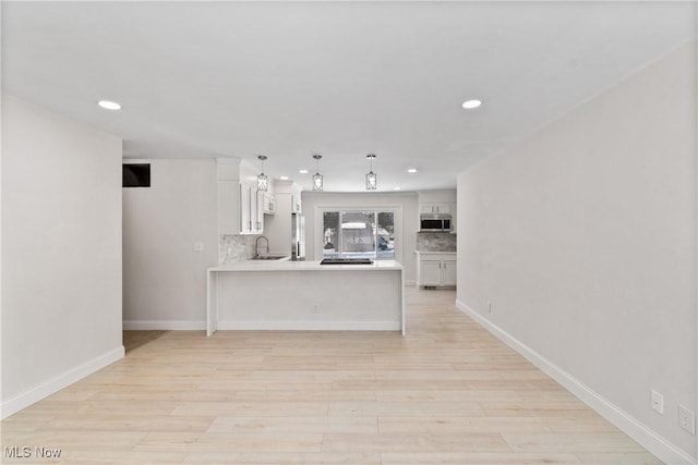 kitchen with tasteful backsplash, kitchen peninsula, sink, stainless steel appliances, and white cabinets