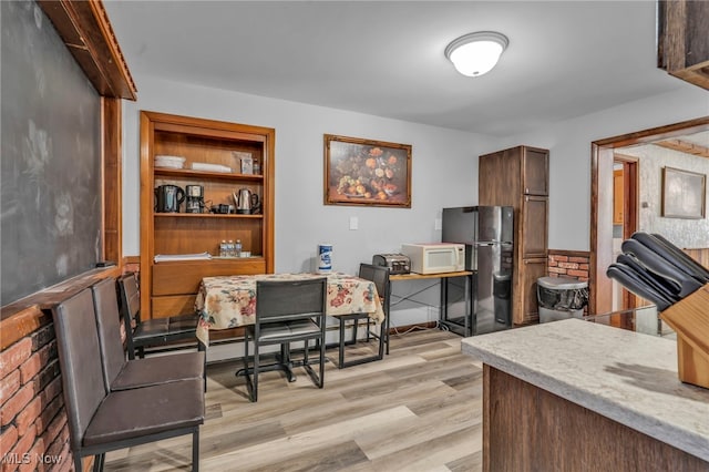 kitchen featuring light wood-type flooring, built in features, a baseboard heating unit, and black fridge