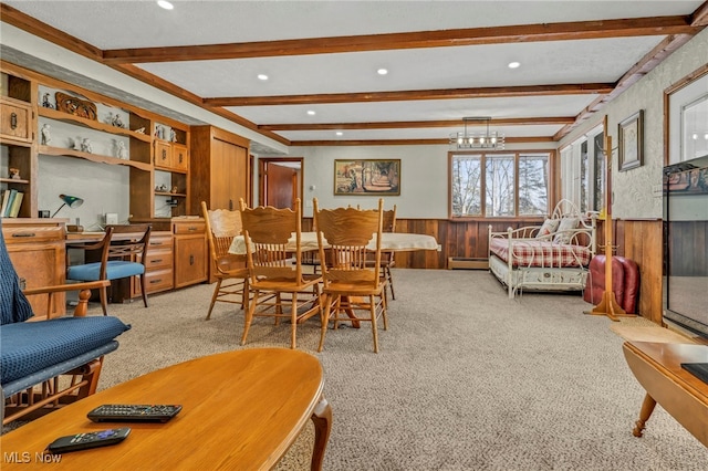 carpeted dining area featuring built in desk, a baseboard heating unit, wood walls, a chandelier, and beam ceiling