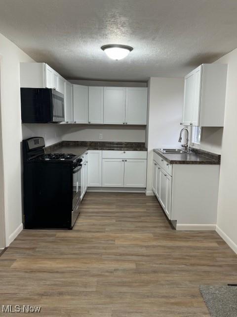 10630 Valley St, Trimble, OH 45782 - kitchen featuring black gas range, white cabinetry, hardwood / wood-style flooring, a textured ceiling, and sink