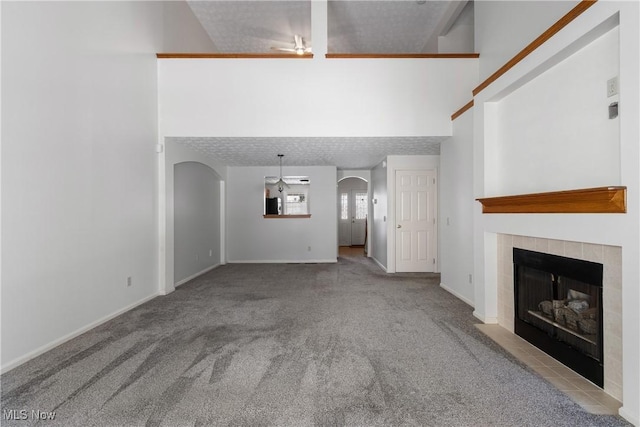 2834 Caxton Cir, Akron, OH 44312 - unfurnished living room with carpet floors, arched walkways, baseboards, a towering ceiling, and a tile fireplace
