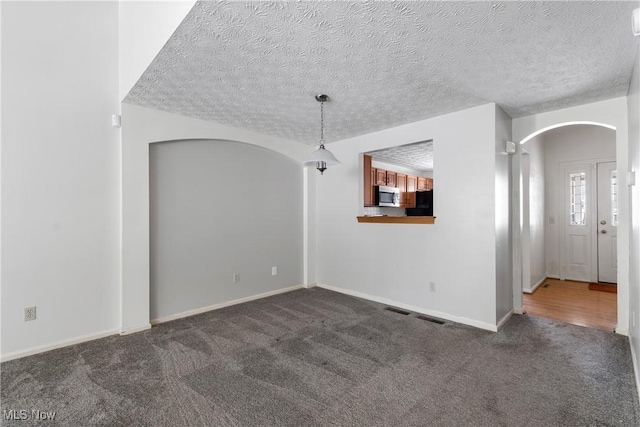 unfurnished room with a textured ceiling and dark colored carpet