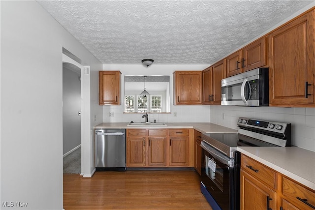 kitchen featuring hardwood / wood-style floors, stainless steel appliances, tasteful backsplash, decorative light fixtures, and sink