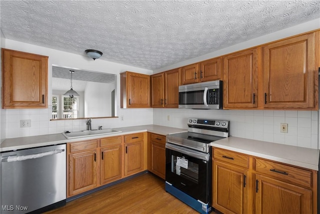 kitchen featuring appliances with stainless steel finishes, decorative backsplash, light wood-type flooring, hanging light fixtures, and sink