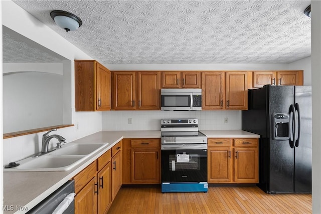 kitchen with backsplash, appliances with stainless steel finishes, sink, and light hardwood / wood-style flooring