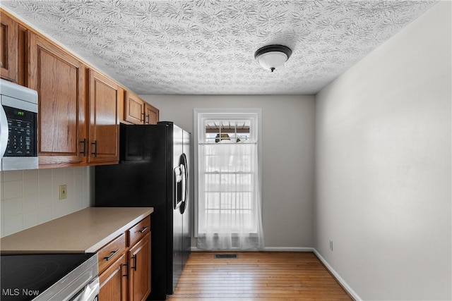 kitchen featuring decorative backsplash, a wealth of natural light, appliances with stainless steel finishes, and light wood-type flooring