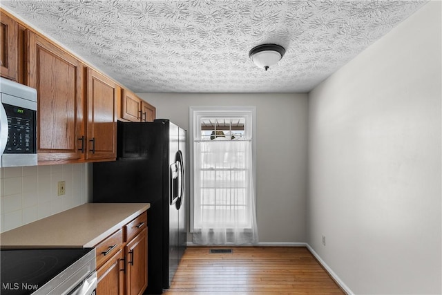 2834 Caxton Cir, Akron, OH 44312 - kitchen with appliances with stainless steel finishes, brown cabinetry, light wood finished floors, decorative backsplash, and baseboards