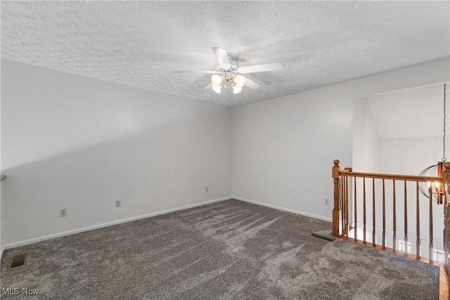 empty room with a textured ceiling, ceiling fan with notable chandelier, and dark carpet