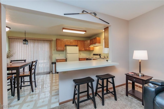 kitchen with white fridge, kitchen peninsula, electric range, decorative light fixtures, and sink