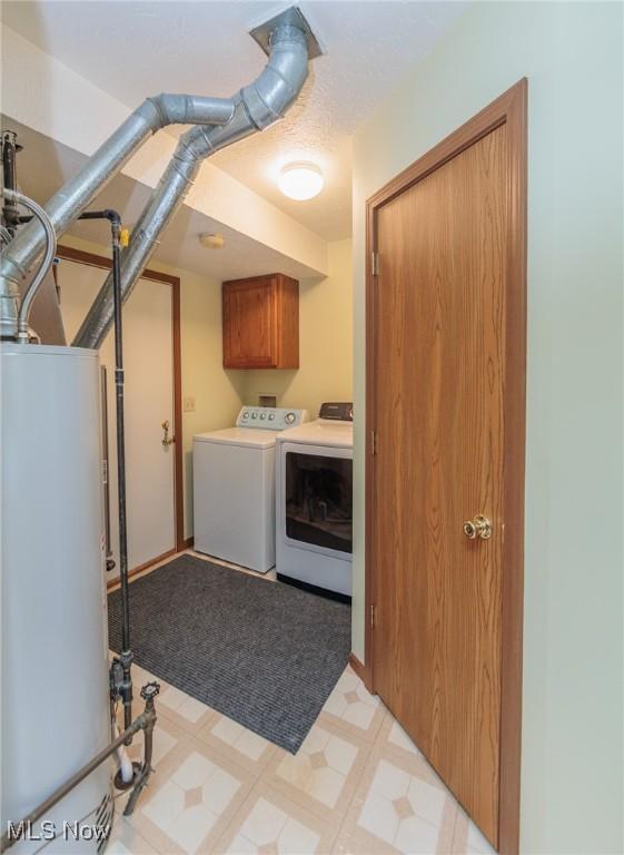 washroom with cabinets, gas water heater, and washing machine and dryer