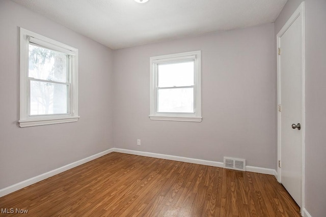 empty room with a wealth of natural light and hardwood / wood-style flooring