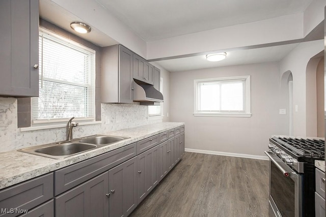 kitchen featuring stainless steel gas stove, sink, backsplash, and gray cabinetry