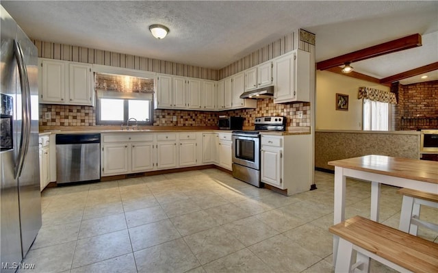 kitchen with beamed ceiling, appliances with stainless steel finishes, white cabinets, and sink