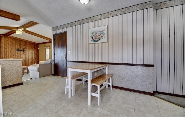 unfurnished dining area with a textured ceiling, vaulted ceiling with beams, and wooden walls