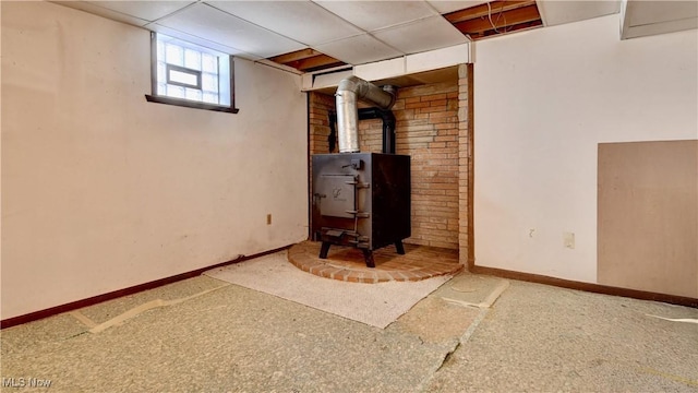 basement with a paneled ceiling, carpet, and a wood stove