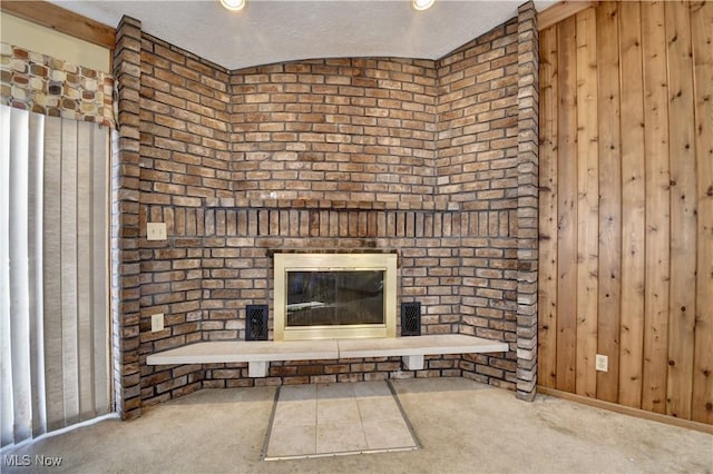 unfurnished living room with carpet flooring, lofted ceiling, a fireplace, and wooden walls