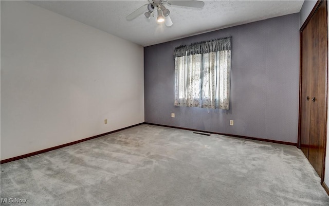 unfurnished bedroom featuring ceiling fan, a textured ceiling, a closet, and light carpet